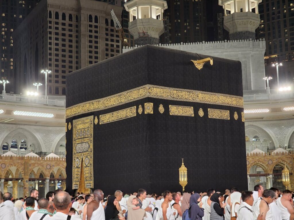 Pilgrims gathered around the Kaaba in Mecca, Saudi Arabia, illuminated at night. A scene of reverence and spirituality.