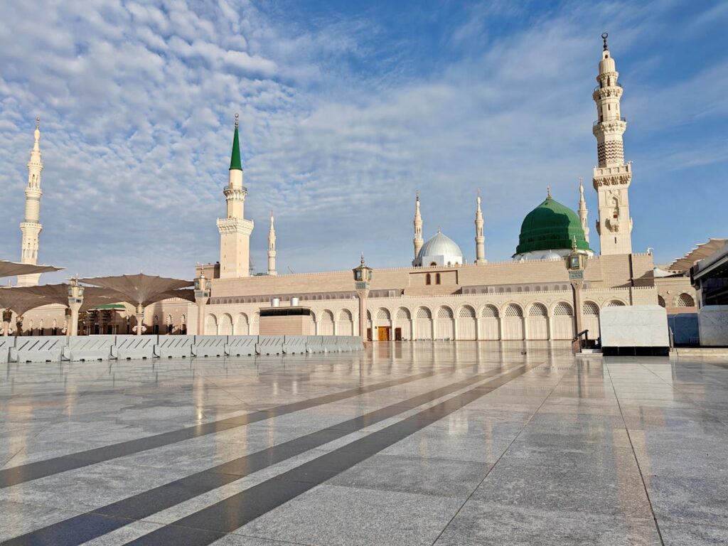 Stunning daytime view of Al-Masjid an-Nabawi Mosque, showcasing its majestic architecture under a blue sky in Medina, Saudi Arabia.